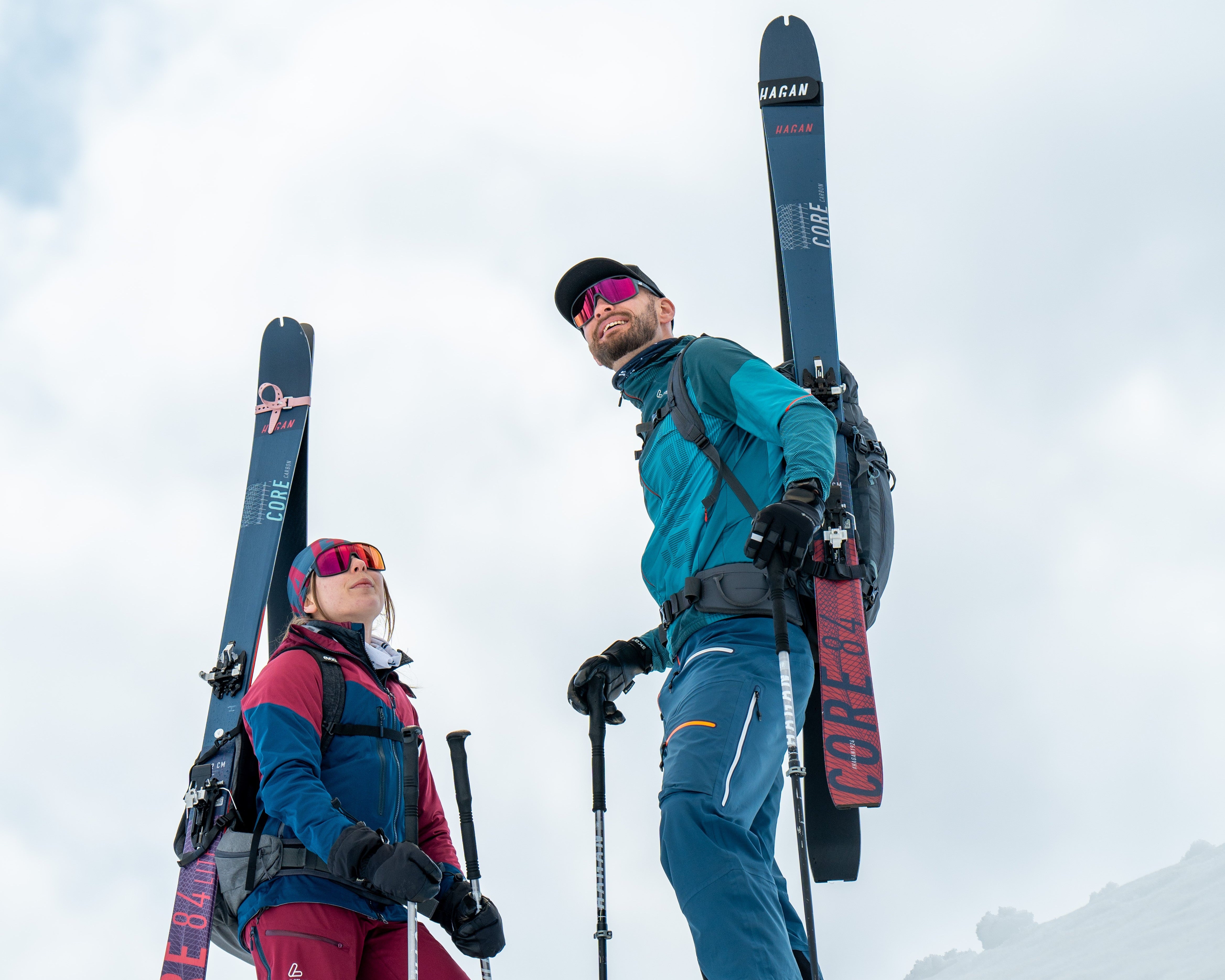 Two skiers standing on a snowy slope with their skis and backpacks.