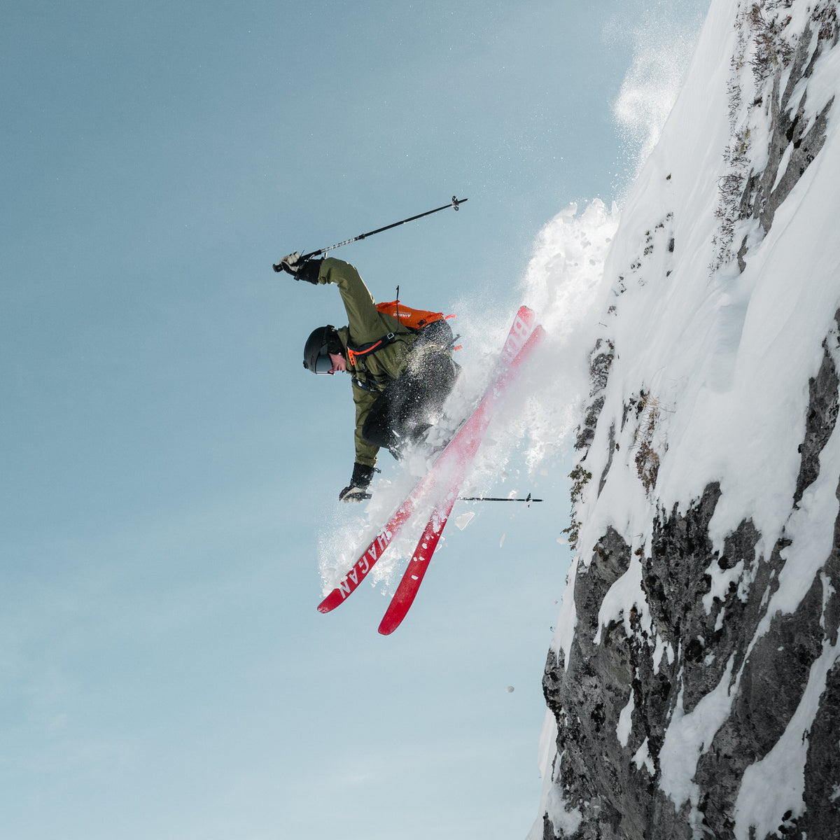 Skier performing a jump off a snowy cliff with mountains in the background