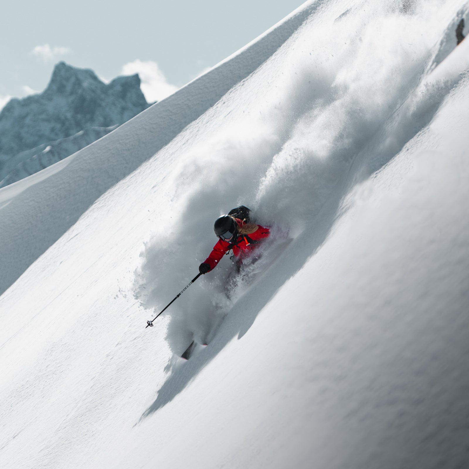 Person skiing down a snowy mountain with mountains in the background